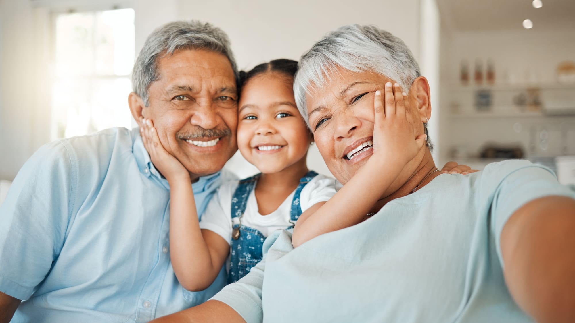 Abuelos sonrientes abrazando a su nieta en la sala de su casa