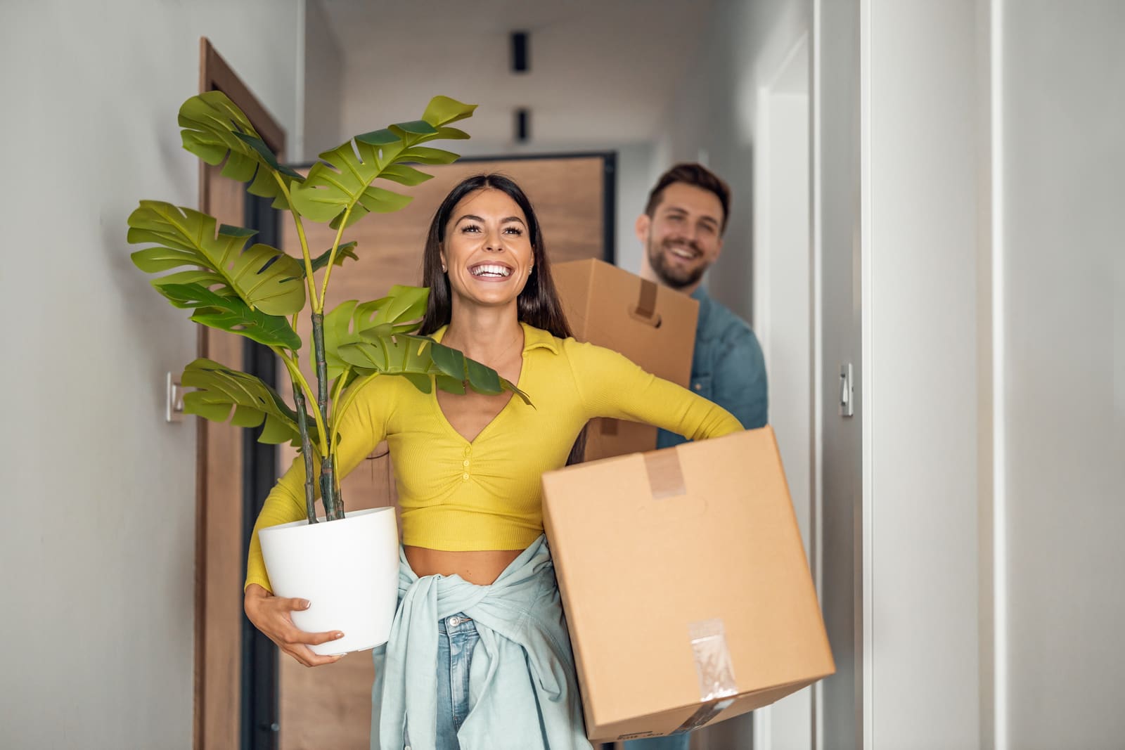 Pareja joven entrando a su casa nueva cargando cajas de mudanza y una planta