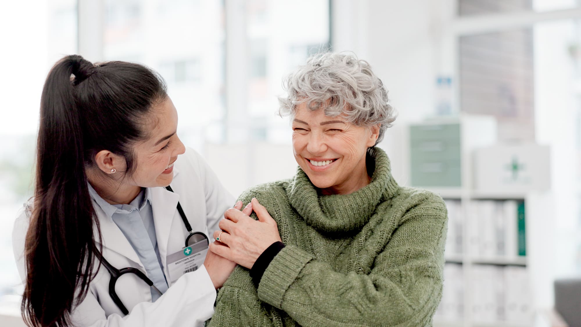 Doctora sonriendo mientras acompaña a una paciente mayor en el consultorio