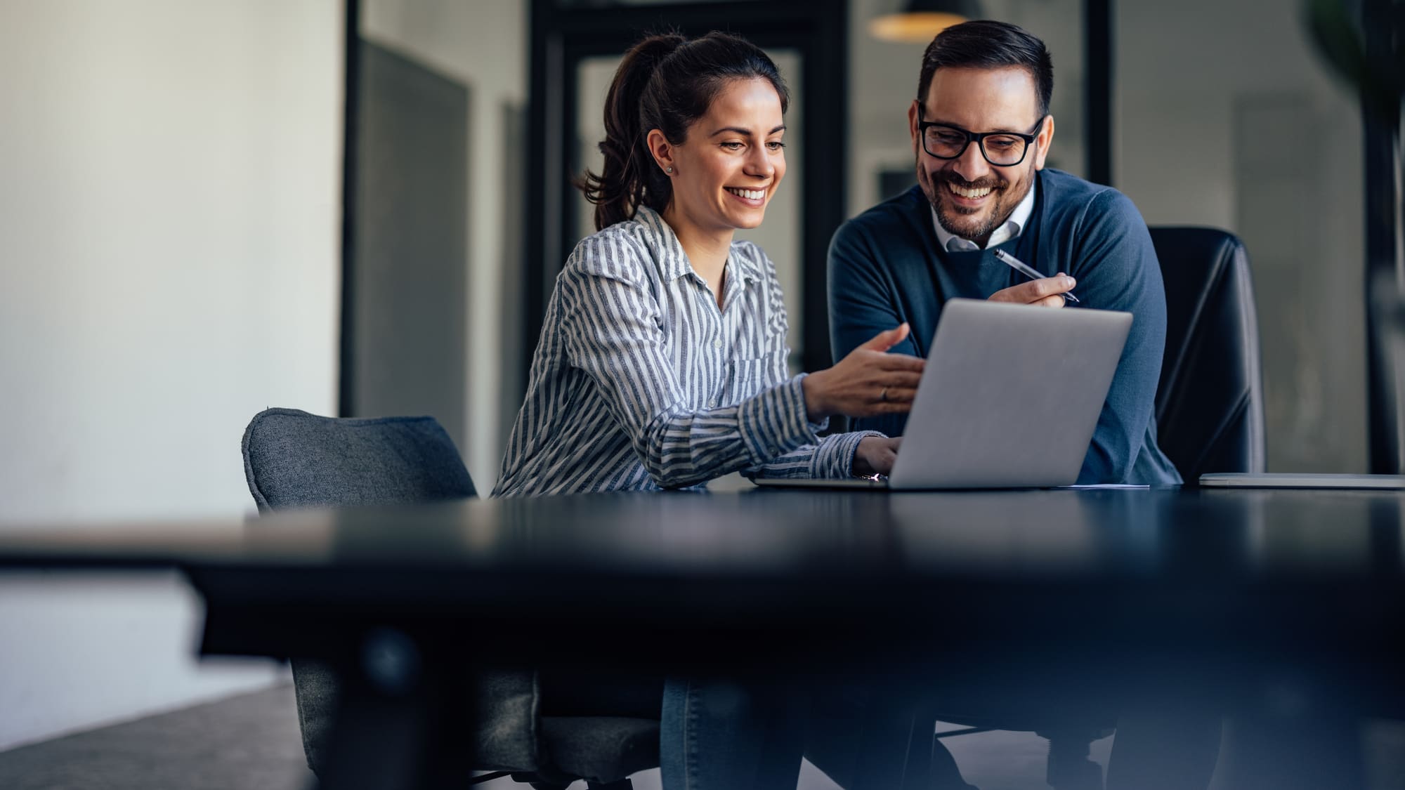 Dos personas revisando juntas un plan financiero en una laptop, sonriendo en una oficina