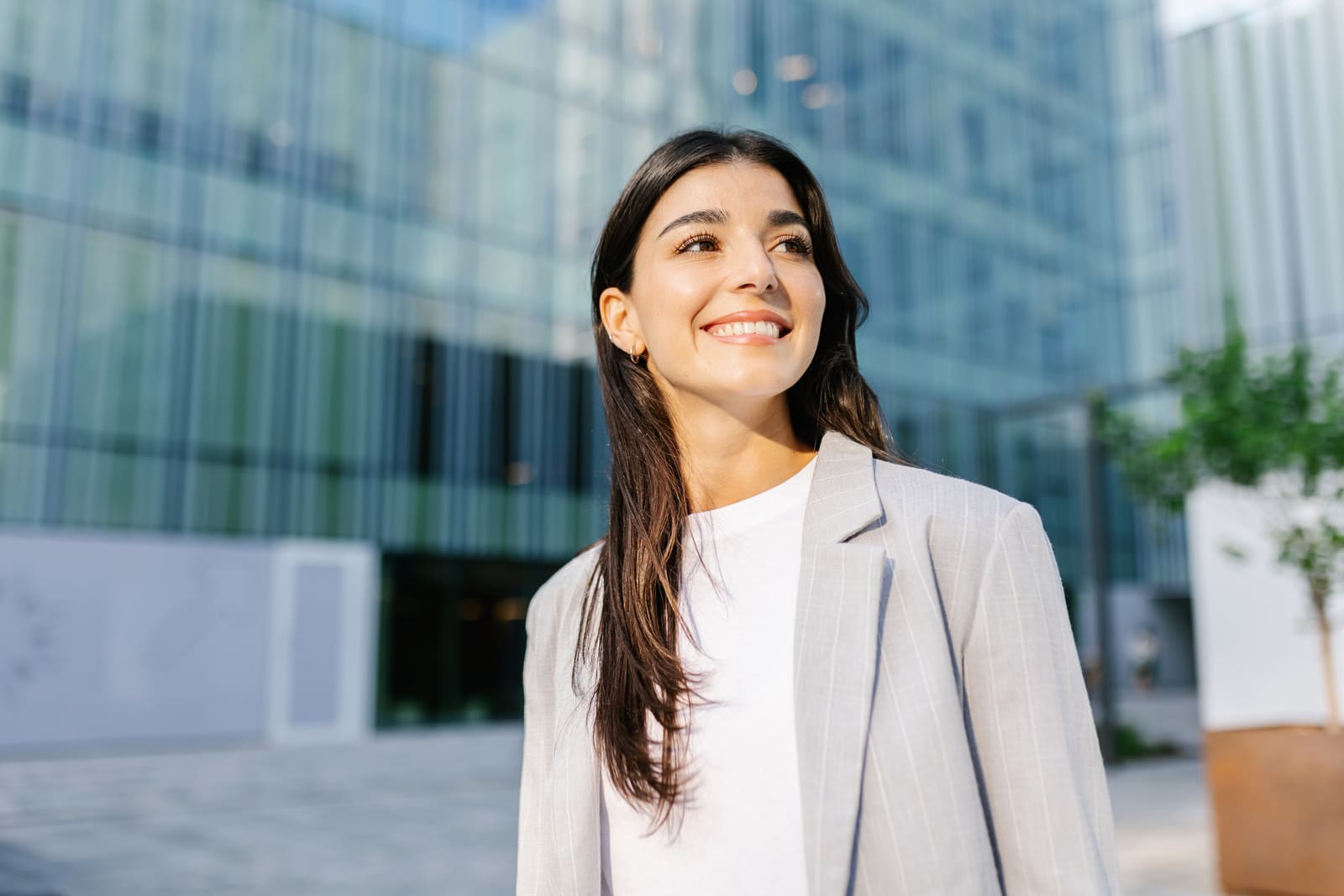 Mujer profesional joven caminando frente a un edificio de oficinas, sonriendo